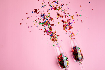 Multi colored confetti and champagne flutes isolated against pink background, copy space