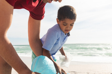 Obraz premium father and son collecting plastic garbage together at beach on sunny day