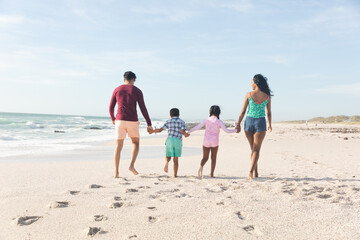 Obraz premium Full length of multiracial family holding hands together walking on sand with footprints at beach