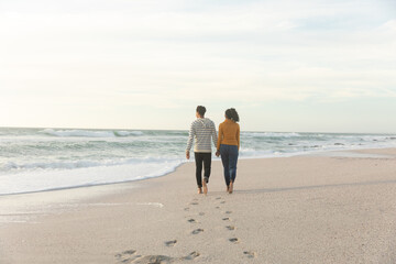 Obraz premium Full length rear view of couple walking while leaving footprints on sand at beach