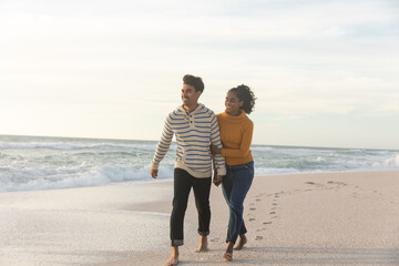 Obraz premium Full length of happy multiracial couple walking on shore at beach against sky during sunset