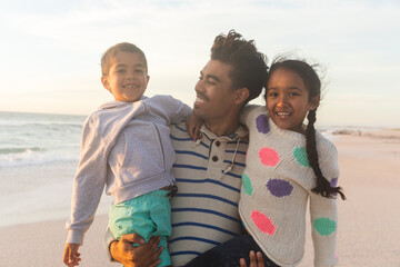 Obraz premium Happy father carrying children while standing at beach against sky during sunset