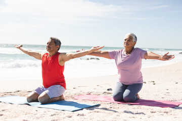 senior couple kneeling while practicing yoga with arms outstretched on mats at sunny beach