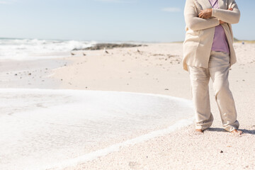 Low section of senior woman standing with arms crossed on shore at beach during sunny day