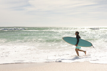 Side view of senior man running with surfboard on shore at beach during sunny day