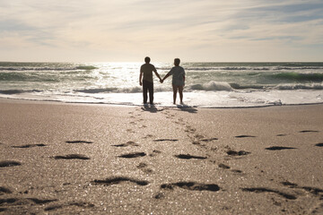 Naklejka premium Footprints on sand with multiracial senior couple holding hands standing at beach during sunny day
