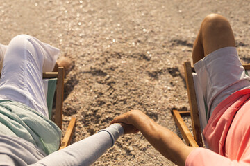 Naklejka premium High angle view of senior multiracial couple holding hands while relaxing on chairs at beach