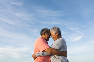 Fototapeta premium Loving senior couple embracing each other while touching foreheads against sky
