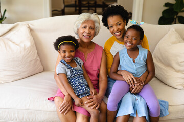 Portrait of smiling african american grandmother, mother and two granddaughters sitting on couch