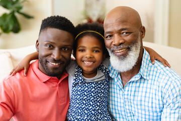 Portrait of african american grandfather, father and granddaughter smiling sitting on couch at home