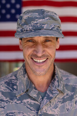 Portrait of smiling caucasian army soldier wearing cap and camouflage uniform against usa flag