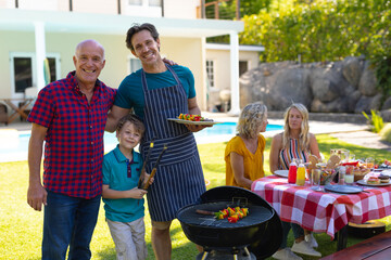 Portrait of caucasian grandfather, father and son barbecuing in the garden