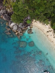 Top down vertical view of crystal clear blue water, rocks, beach and coastal vegetation