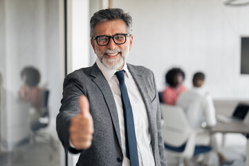 Senior businessman giving confident thumbs up in office