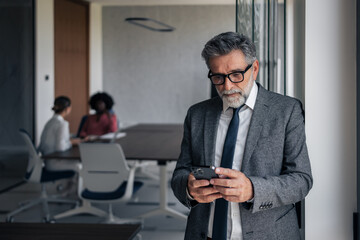 Senior businessman using smartphone in modern corporate office