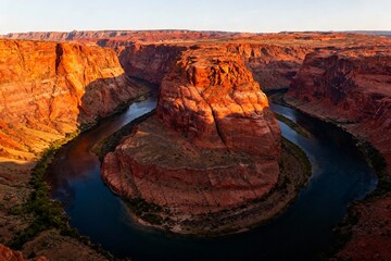 Aerial view of a river forming a horseshoe bend through red rock canyon at sunset
