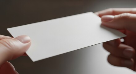 Obraz premium Professional hands presenting a blank white textured business card mockup template on a dark background, ideal for corporate branding identity showcase.