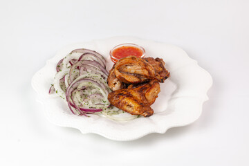 Close-up of grilled chicken wings with onions and sauce on white plate