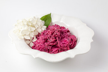 Close-up of beet and cabbage salad in white bowl with floral garnish