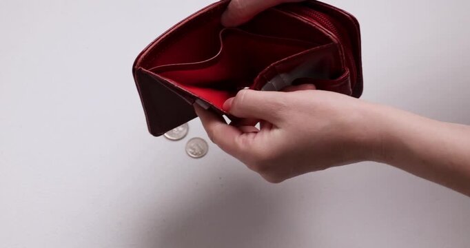 Person opens a small, shiny, red wallet on a white table. Inside, it is mostly empty with only a few coins. The wallet is then closed and rests on the table.