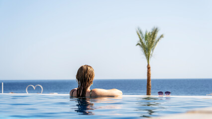 Woman in the pool by the beach looking at the sea
