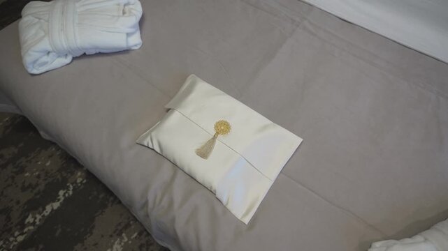 Textile envelope with fresh towels rests on neatly made bed. Soft textures and clean arrangement enhance cozy hotel room atmosphere