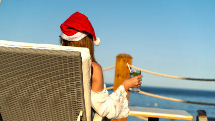 Woman in Santa Claus cap by the sea on a sun lounger