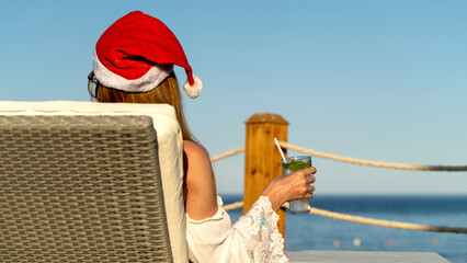 Woman in Santa Claus cap by the sea on a sun lounger