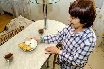 Elderly woman placing sweet pastries and tea on table for guests, gentle smile, calm anticipation, warm domestic setting, hospitality, family gathering, cozy home atmosphere