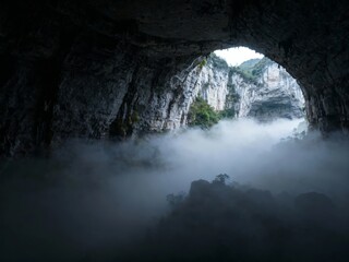 Mist-filled cave entrance revealing rocky landscape and distant cliffs