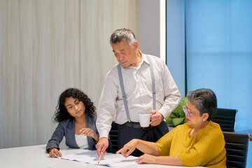 Senior businessman manager working with his team for point to something on the paper in co-working space.