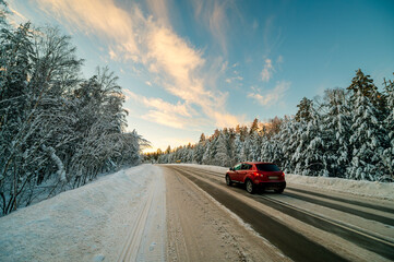 a red car is driving on a winter road, with white snow-covered Christmas trees on the side
