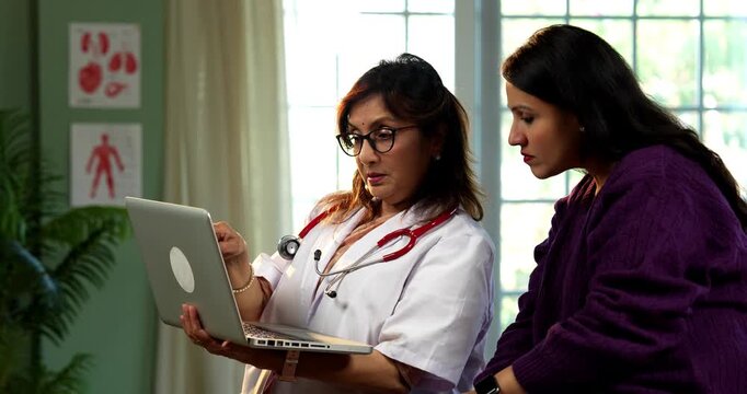 Indian lady doctor and female patient discussing case on laptop during detailed consultation in modern clinic, showing senior expertise, digital healthcare workflow, patient focused medical guidance