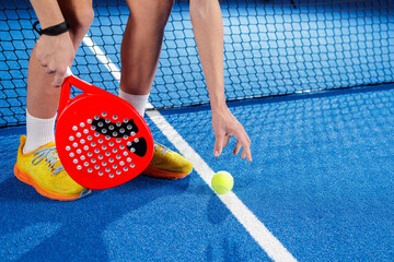 Padel player drops ball for serve on blue indoor court close up