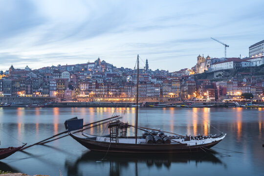 View of a traditional Portuguese Rabelo boat floats serenely on the Douro River, reflecting the warm glow of Porto's illuminated cityscape, Porto, Porto District, Portugal.
