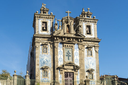 View of the  facade of the Church of Saint Ildefonso with detailed stonework, crosses, and blue and white tile panels under a clear sky, Porto, Porto District, Portugal.