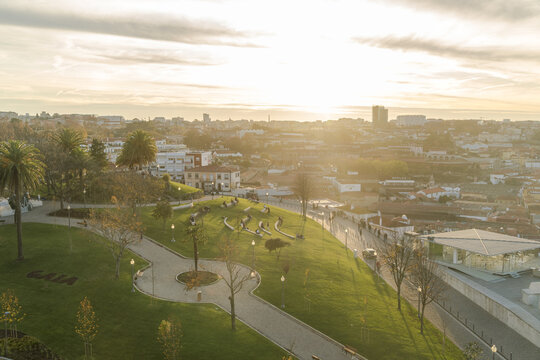 View of a vibrant Jardim do Morro park contrasted against the golden cityscape as sunlight bathes everything in a warm glow, Porto, Porto District, Portugal.