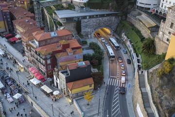 View of terra cotta rooftops cascading down to a bustling street lined with vibrant stalls and traffic flowing through a stone tunnel, Porto, Porto District, Portugal.