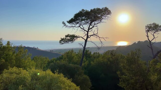 People are watching the sunset on the sand dunes of the Mediterranean coast at Patara Beach, Turkey. Sunset on the sand dunes of Patara. Desert with dunes, a mountain range, and a blue sea. Bright sun