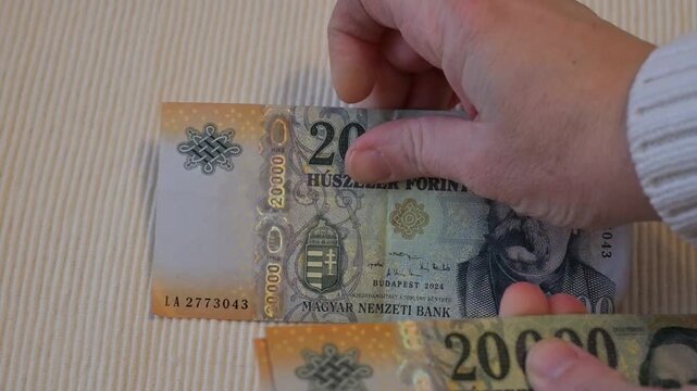 Female hand counting Hungarian forint banknotes on white background. Financial control, accounting, budgeting, salary management, and money handling concept.