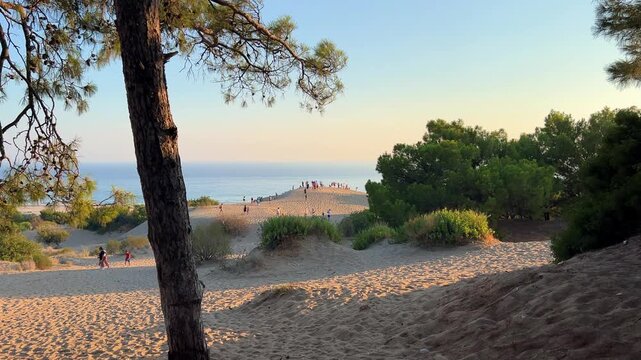 People are watching the sunset on the sand dunes of the Mediterranean coast at Patara Beach, Turkey. Sunset on the sand dunes of Patara. Desert with dunes, a mountain range, and a blue sea. Bright sun