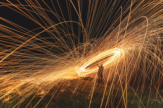 View of sparks of light dance in the dark, painting fiery circles above the grassy ground with a silhouette of a person, Isle of Skye, United Kingdom.