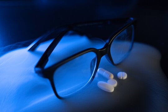 Niebieski dym na czarnym tle, okulary w czarnej oprawie i tabletki