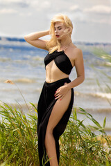 Blonde woman in black dress on windy seaside dunes