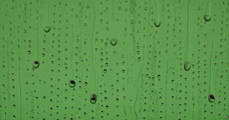 Close up of wet glass with dripping water drops and streaks of rain, on a bright green chroma key background, perfect for visual effects and background replacement. Slow motion. - Powered by Adobe
