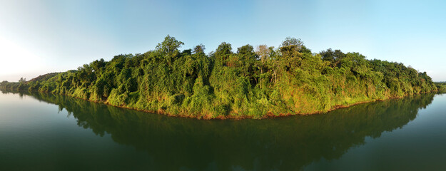 panorama of river bank with rainforest and thick jungle reflected in water. Morning light is is clear and warm.
