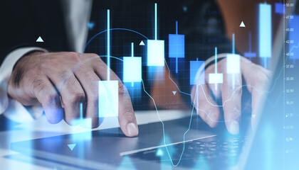 Businessman's hands using laptop with glowing stock market candlestick chart hologram overlay representing forex and crypto trading data analysis concept.