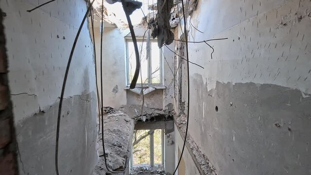 Extensive structural damage to a residential building featuring holes in the roof and ceilings, blown-out doors, and shrapnel marks on walls after an airstrike