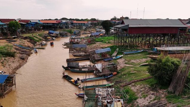 Aerial view of kampong phluk, a floating village with stilt houses built along a river surrounded by green rice paddies.