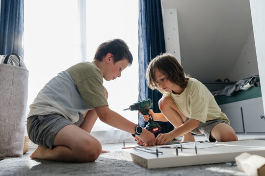 Children assembling flat pack furniture using a power drill